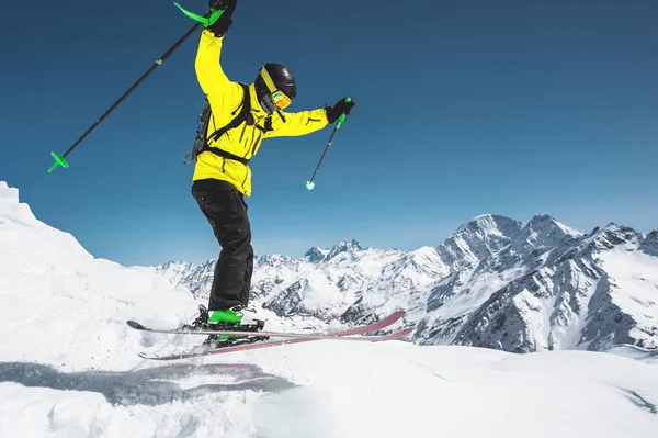 Um esquiador em equipamento desportivo completo salta para o abismo do topo da geleira contra o fundo do céu azul e as montanhas cobertas de neve caucasianas. Vista pelas traseiras. Região de Elbrus — Fotografia de Stock