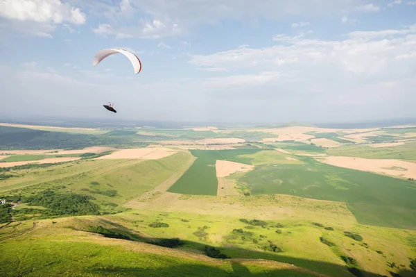 Un parapente blanco-naranja vuela sobre el terreno montañoso — Foto de Stock