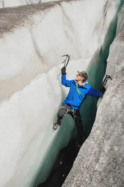 Um escalador livre sem seguro com dois machados de gelo sobe de uma rachadura na geleira. Escalada livre sem cordas — Fotografia de Stock