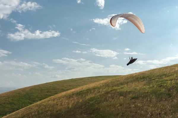 Ein weiß-orangefarbener Gleitschirm fliegt über das bergige Gelände — Stockfoto