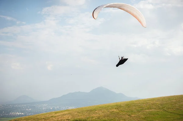 Ein weiß-orangefarbener Gleitschirm fliegt über das bergige Gelände — Stockfoto