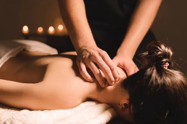 Mens händer gör en terapeutisk hals massera för en flicka som ligger på en massage soffa i en massage spa med mörka belysning. Närbild. Mörka nyckel — Stockfoto