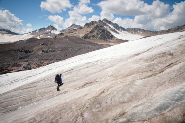 Bir sırt çantası ile bir dağcı çatlaklar dağ arasında elinde kaldırımlar ile tozlu bir buzul boyunca yürüyüş krampon içeri girer