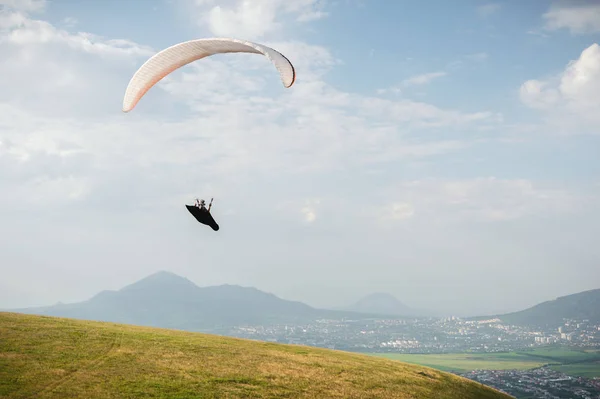 A white-orange paraglider flies over the mountainous terrain — Stock Photo, Image