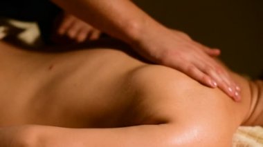 Yakın çekim spa masaj kadının omuz ve sırt. Erkek el mum içinde belgili tanımlık geçmiş ile karanlık bir odada bir kadına masaj