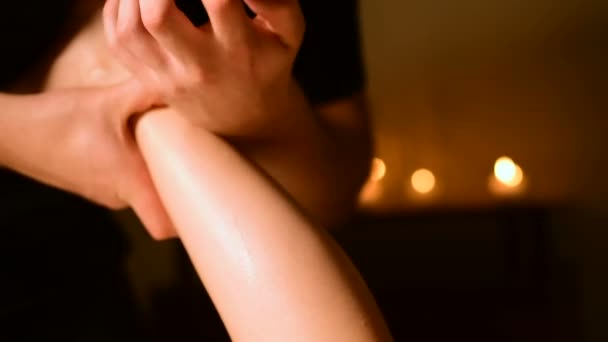 Massage des unteren Teils des weiblichen Beines mit Öl auf dem Hintergrund von Kerzen in einem dunklen Raum — Stockvideo