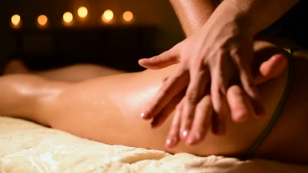 Voor een vrouw doet een masseur in een donkere kamer een hip massage met olie. Spa procedures massage vrouwen — Stockvideo
