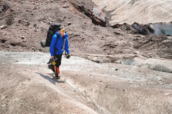 Um montanhista com uma mochila caminha em crampons andando ao longo de uma geleira empoeirada com calçadas nas mãos entre rachaduras na montanha — Fotografia de Stock