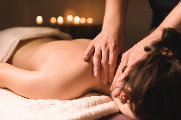 Mens handen maken een therapeutische nek massage voor een meisje liggend op een massage Bank in een massage spa met donkere verlichting. Close-up. Donkere sleutel — Stockfoto