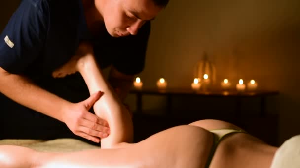 Massage of the lower part of the female leg with oil on the background of candles in a dark room — Stock Video