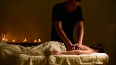 Yakın çekim spa masaj kadının omuz ve sırt. Erkek el mum içinde belgili tanımlık geçmiş ile karanlık bir odada bir kadına masaj
