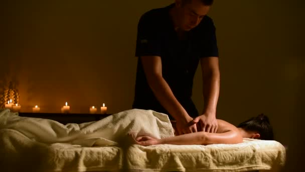 Primo piano spa massaggio donne spalle e schiena. Le mani maschili massaggiano una donna in una stanza buia con candele sullo sfondo — Video Stock