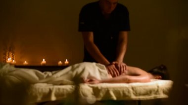 Yakın çekim spa masaj kadının omuz ve sırt. Erkek el mum içinde belgili tanımlık geçmiş ile karanlık bir odada bir kadına masaj
