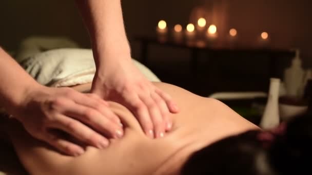 Крупним планом чоловічі руки роблять цілющий масаж з маслом для молодої дівчини в темному кабінеті косметології. Темна клавіша — стокове відео