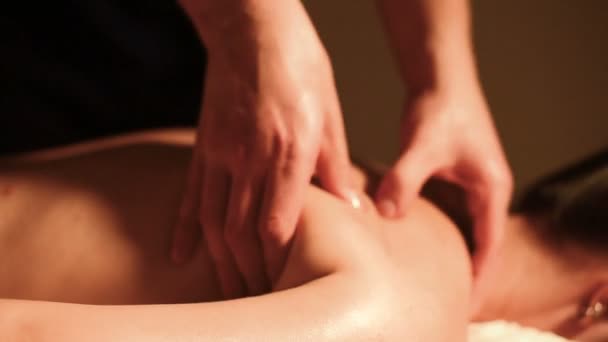 Gros plan mains masculines faisant massage curatif à l'huile à une jeune fille dans un bureau de cosmétologie sombre. Clé sombre — Video