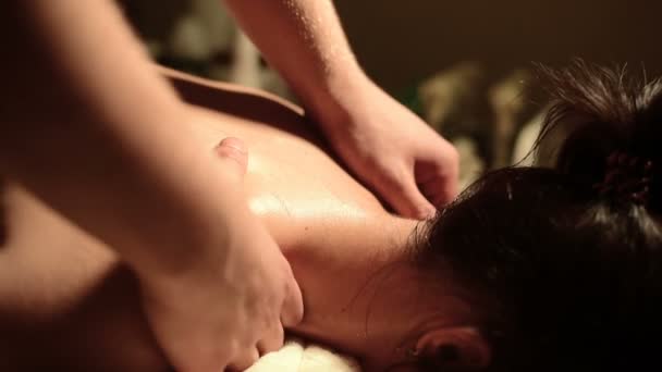 Een jonge vrouw ontvangt een massage van een mans handen in een kamer met een donker licht. Close-up. Soft Focus Sea... — Stockvideo