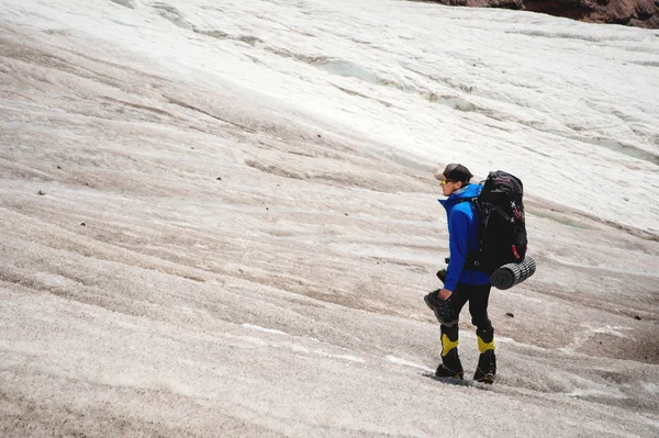 Bir dağcı bir sırt çantası ile tekerlekli sandalye yürür, spor ayakkabı içinde çatlaklar dağlarda arasında el ile tozlu bir buzulun üzerinde duruyor