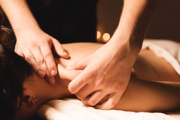 Mens händer gör en terapeutisk hals massera för en flicka som ligger på en massage soffa i en massage spa med mörka belysning. Närbild. Mörka nyckel — Stockfoto