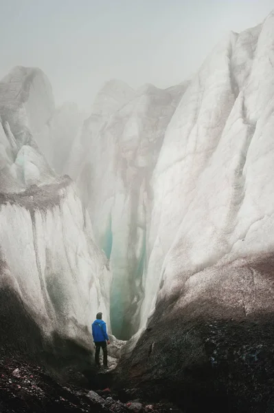 Свободный альпинист с ледорубом в руке стоит у подножия Большого ледника рядом с эпической трещиной в тумане в горах. Неодолимое препятствие — стоковое фото