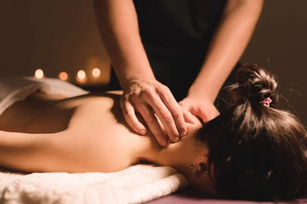 Mens händer gör en terapeutisk hals massera för en flicka som ligger på en massage soffa i en massage spa med mörka belysning. Närbild. Mörka nyckel — Stockfoto