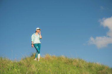 Fitness runner kadın niteliğine müzik dinlemek. Kulaklık Kulaklık giyen ve kap çalışan güzel kız portresi. bir yeşil alan ve mavi gökyüzü arka planı