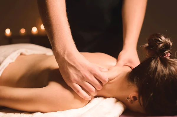 Mens handen maken een therapeutische nek massage voor een meisje liggend op een massage Bank in een massage spa met donkere verlichting. Close-up. Donkere sleutel — Stockfoto