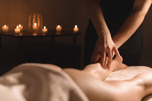 Primer plano de las manos masculinas haciendo masaje de pantorrilla de piernas femeninas en una habitación oscura con velas en el fondo. Cosmetología y tratamientos de spa — Foto de Stock