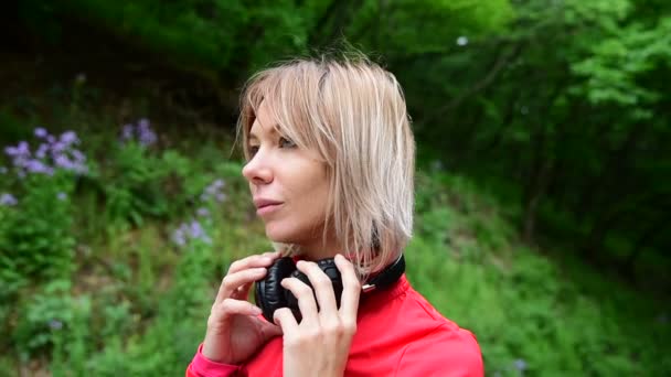 Gros plan d'une jolie blonde portant des écouteurs pour faire du jogging à l'extérieur dans la forêt — Video