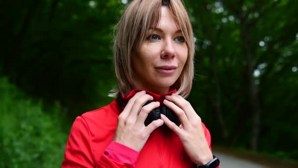 Close-up van een mooi blond meisje dragen koptelefoon om te joggen buiten in het bos — Stockvideo
