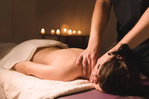 Männerhände machen eine therapeutische Nackenmassage für ein Mädchen, das auf einer Massageliege in einem Massagebad mit dunkler Beleuchtung liegt. Nahaufnahme. dunkler Schlüssel — Stockfoto