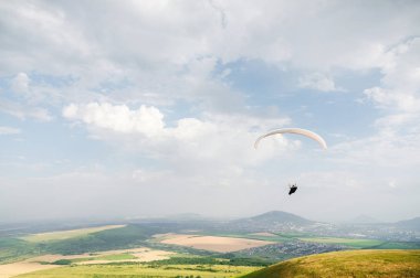 Beyaz-turuncu yamaçparaşütü dağlık arazi üzerinde uçar