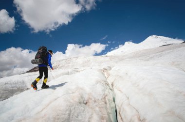 Bir sırt çantası ile bir dağcı çatlaklar dağ arasında elinde kaldırımlar ile tozlu bir buzul boyunca yürüyüş krampon içeri girer