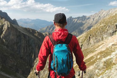 Sakallı bir adam güneş gözlüğü ve bir sırt çantası ile bir kap içinde bir kaya üzerine anlamına gelir ve bir kayalık vadide yüksek dağların içine görünüyor. Turizm ve kolay açık dağlarda trekking kavramı.