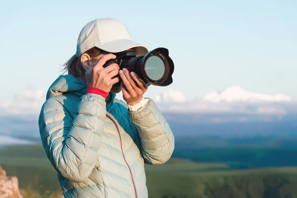 Портрет дівчини-фотографа в кепці на природі, що фотографує її цифрову дзеркальну камеру. Вид спереду — стокове фото