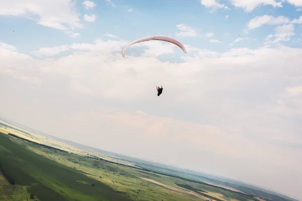 Een wit-oranje paraglider vliegt over het bergachtige terrein — Stockfoto