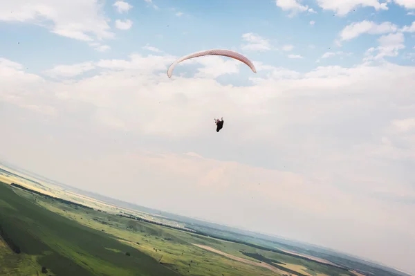 Ein weiß-orangefarbener Gleitschirm fliegt über das bergige Gelände — Stockfoto