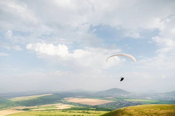 Un parapente blanco-naranja vuela sobre el terreno montañoso — Foto de Stock