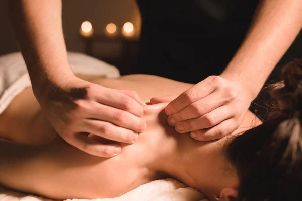 Male manual worker doing spa massage of shoulders and neck to young girl in dark room