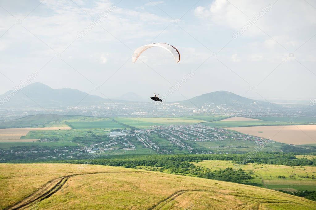 A white-orange paraglider flies over the mountainous terrain.