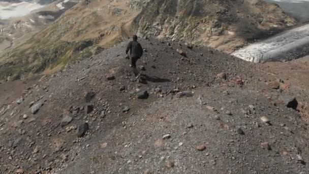 Un joven en las montañas camina sobre una colina en las montañas cubiertas de polvo volcánico y piedras. El concepto de libertad para viajar por las montañas. Vista aérea — Vídeo de stock