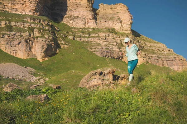 Vonzó sport lány egy sapkát és fejhallgató jogging festői környezetben, a hegyen, közel a sziklák le a naplemente. Edzés a szabadban — Stock Fotó