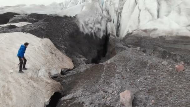 Genç dağcı güneş gözlüklü bir kap ve krampon Kafkasya dağlarında büyük çatlaklar ile büyük bir buzulun üzerinde duruyor. Buzul tarafından volkanik toz pudra — Stok video