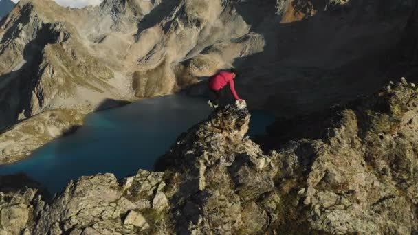 Bir sakallı bir dağcı bir şapka ve güneş gözlüğü, Genç bir adam dağlarda yüksek kayalık bir sırt tırmanıyor. Parkour dağlarda. Arial görünümü — Stok video