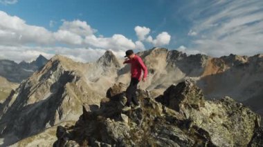 Bir sakallı bir dağcı bir şapka ve güneş gözlüğü, Genç bir adam dağlarda yüksek kayalık bir sırt tırmanıyor. Parkour dağlarda. Arial görünümü