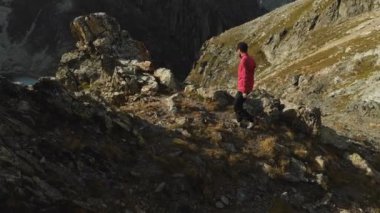 Bir sakallı bir dağcı bir şapka ve güneş gözlüğü, Genç bir adam dağlarda yüksek kayalık bir sırt tırmanıyor. Parkour dağlarda. Arial görünümü