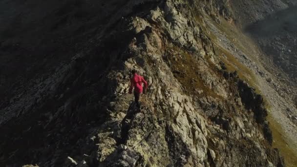 帽子とサングラス 登山家の若い男は 山の高い岩の尾根を登っていきます 山の中のパルクール Arial ビュー — ストック動画