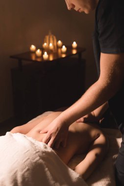 Yakın çekim erkek eller şifa yaparken bir koyu kozmetik ofiste genç bir kız için yağı ile masaj. Karanlık anahtar