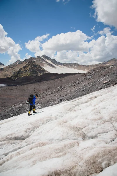 Un montañero con una mochila camina en crampones caminando a lo largo de un glaciar polvoriento con aceras en las manos entre grietas en la montaña —  Fotos de Stock