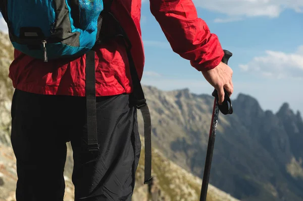 Detailní záběr tělo muže s batohem a jiné-turistické zboží stojí na vrcholu skály proti pozadí skalnatých údolí vysokou v horách. Koncepce cestovního ruchu a snadný trekking v horách — Stock fotografie