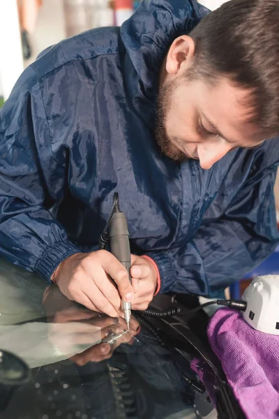 Närbild av bil glasyr arbetare fastställande och reparerar en vindruta eller vindrutan på en bil på en bensinstation i garaget. Borra glas för reparation — Stockfoto